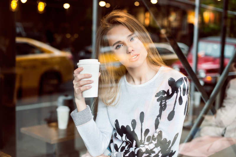 棕色装饰背景下坐在橱窗前喝咖啡的美女