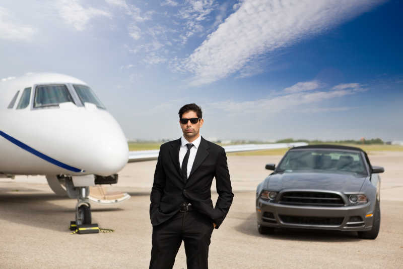 站在汽车和私人飞机前的自信的男性企业家