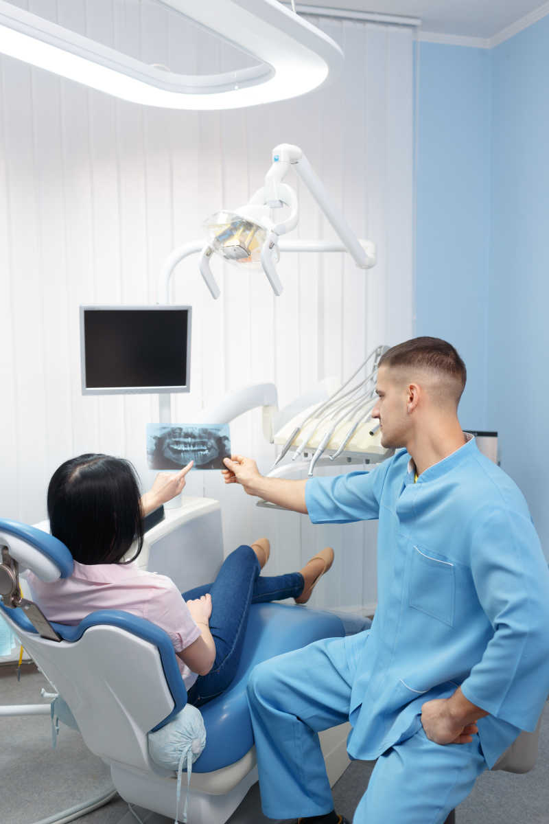 给牙科病人看X光照片的男性牙医