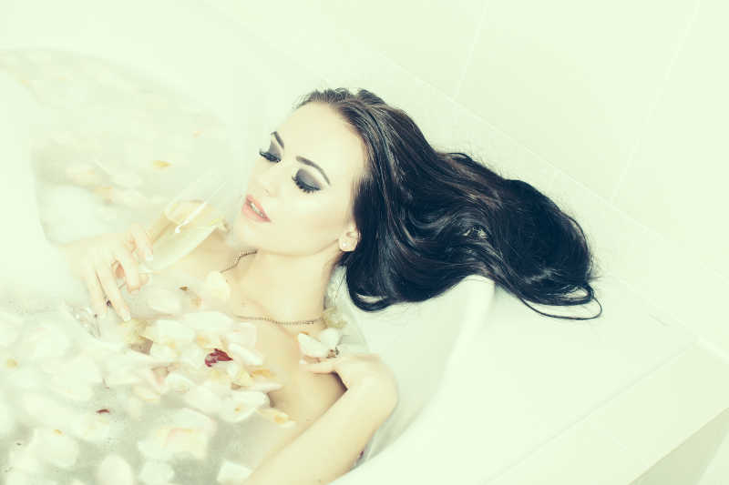 在浴缸内享受花瓣泡澡和香槟的女人
