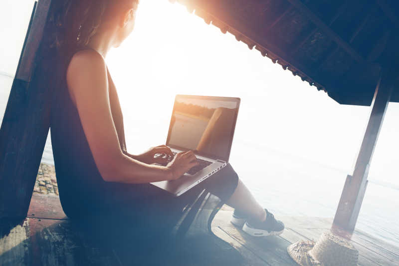 阳光下将笔记本电脑放在腿上工作的女人