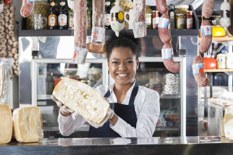 熟食店里黑人女性微笑着拿着奶酪