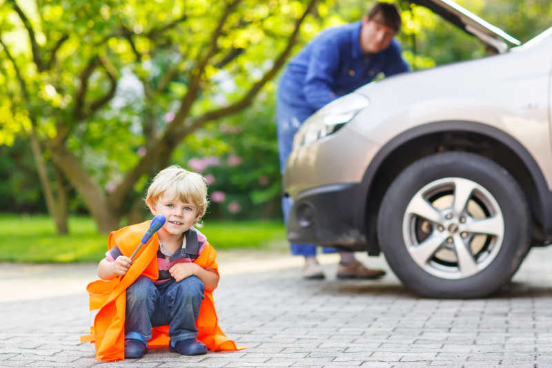 小男孩在他父亲修理汽车的时候穿着橙色的安全背心
