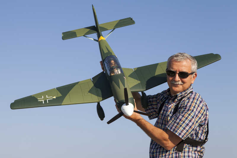 蓝天下老人拿着绿色飞机模型