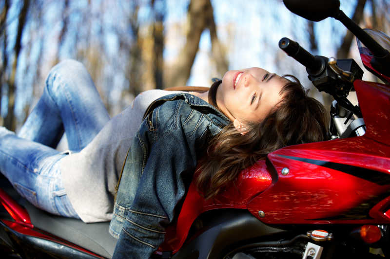 树林里阳光下躺在红色摩托车上的女孩