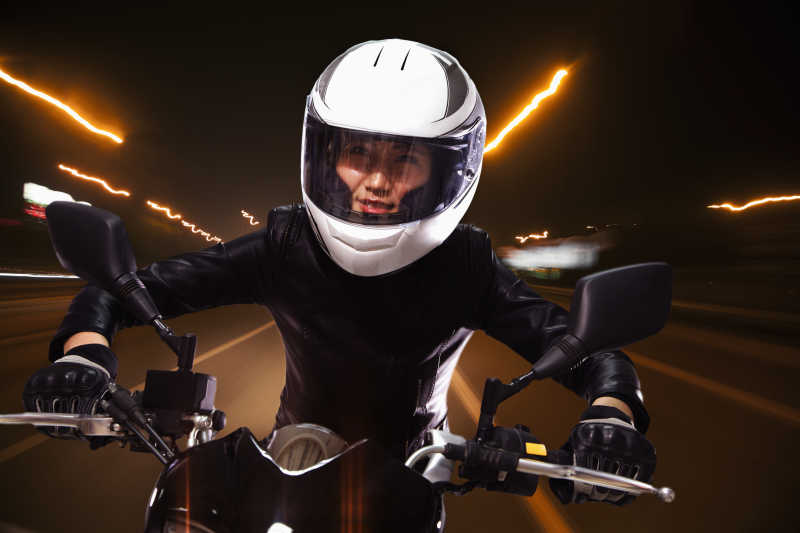 夜色霓虹灯下戴着头盔骑着摩托车的黑衣女子