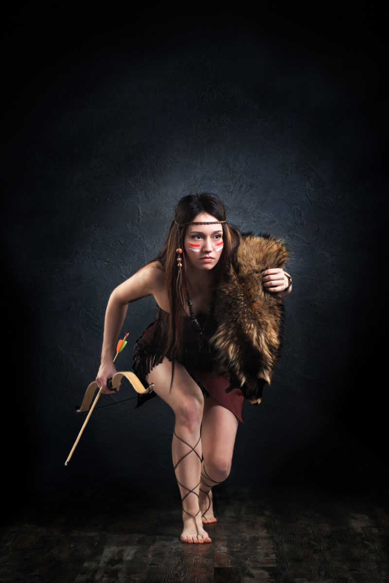 黑色背景下背着猎物拿着弓箭的女猎人