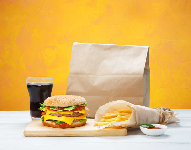 黄色背景下的棕色的包装纸里的汉堡套餐