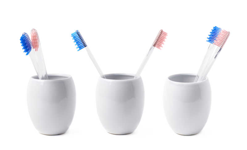 白色背景下三个白色陶瓷杯里的蓝色和粉红色刷毛牙刷