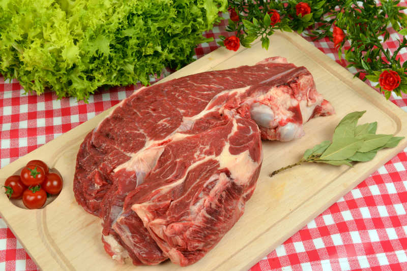 红色格子桌布背景下木砧板上的一块红色瘦牛肉 