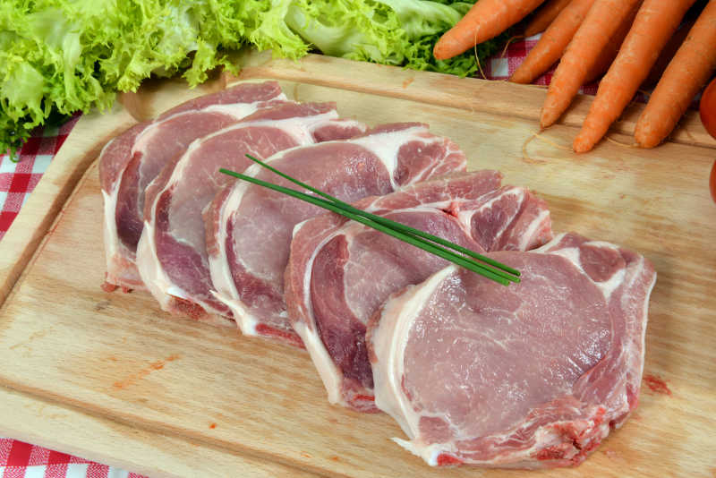 木色砧板上的切好的生猪肉和一些蔬菜