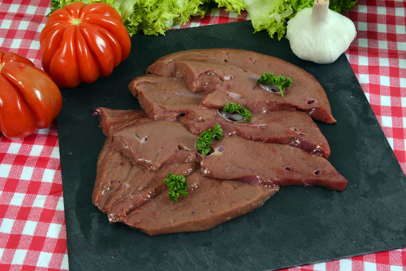 黑色砧板上的一块暗红色的生猪肝和蔬菜