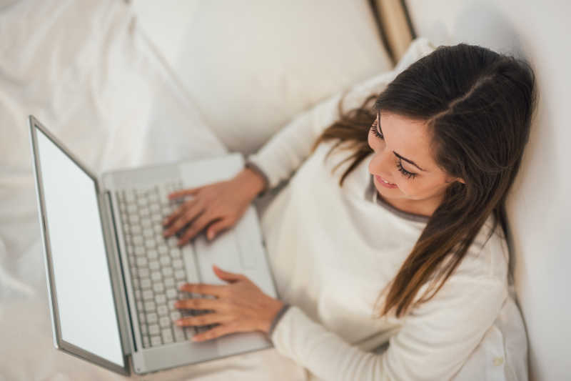 坐在白色床上使用笔记本电脑的女人