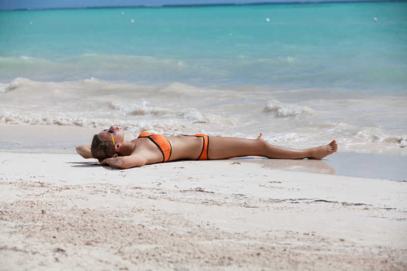 浅绿色海边躺在沙滩上穿着橙色比基尼晒太阳的美女