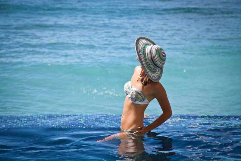 在蓝色游泳池里穿着比基尼戴着太阳帽的美女
