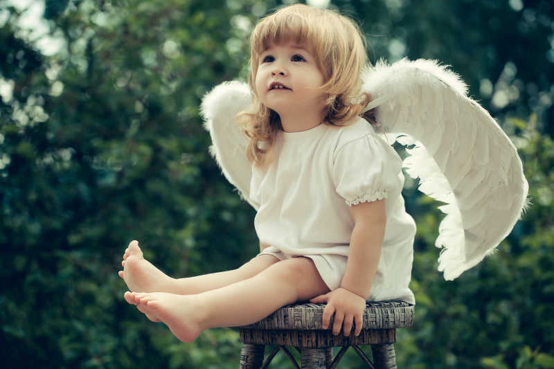 可爱的坐在木椅上的扮成天使的男孩