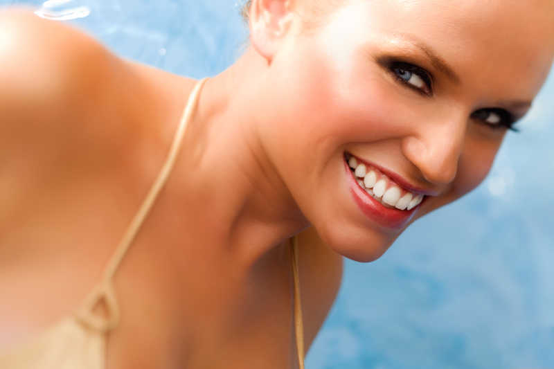 年轻的有健康肌肤的在泳池背景上的女性