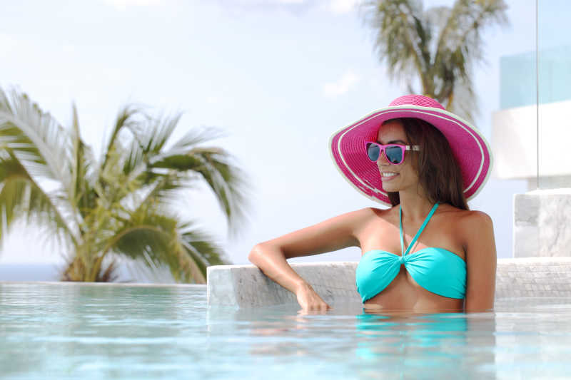 游泳池内性感的女人戴着太阳帽与眼镜