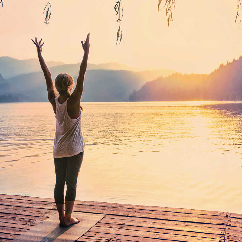 在湖边练瑜伽的年轻女子向太阳致敬