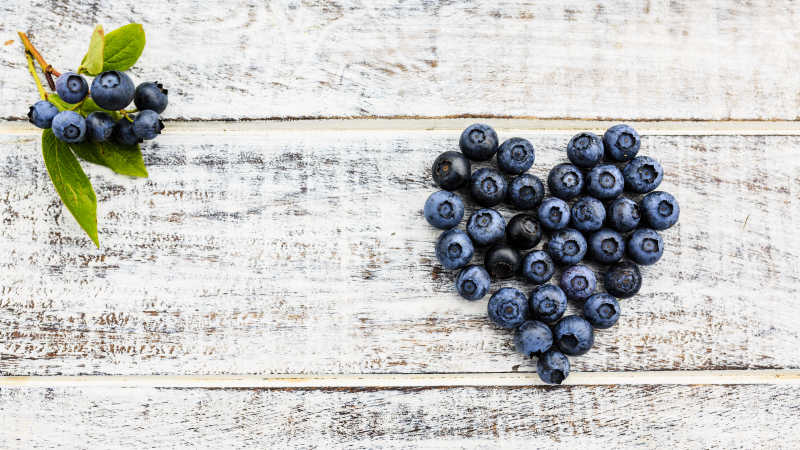 木质板上的心形蓝莓堆和一串蓝莓