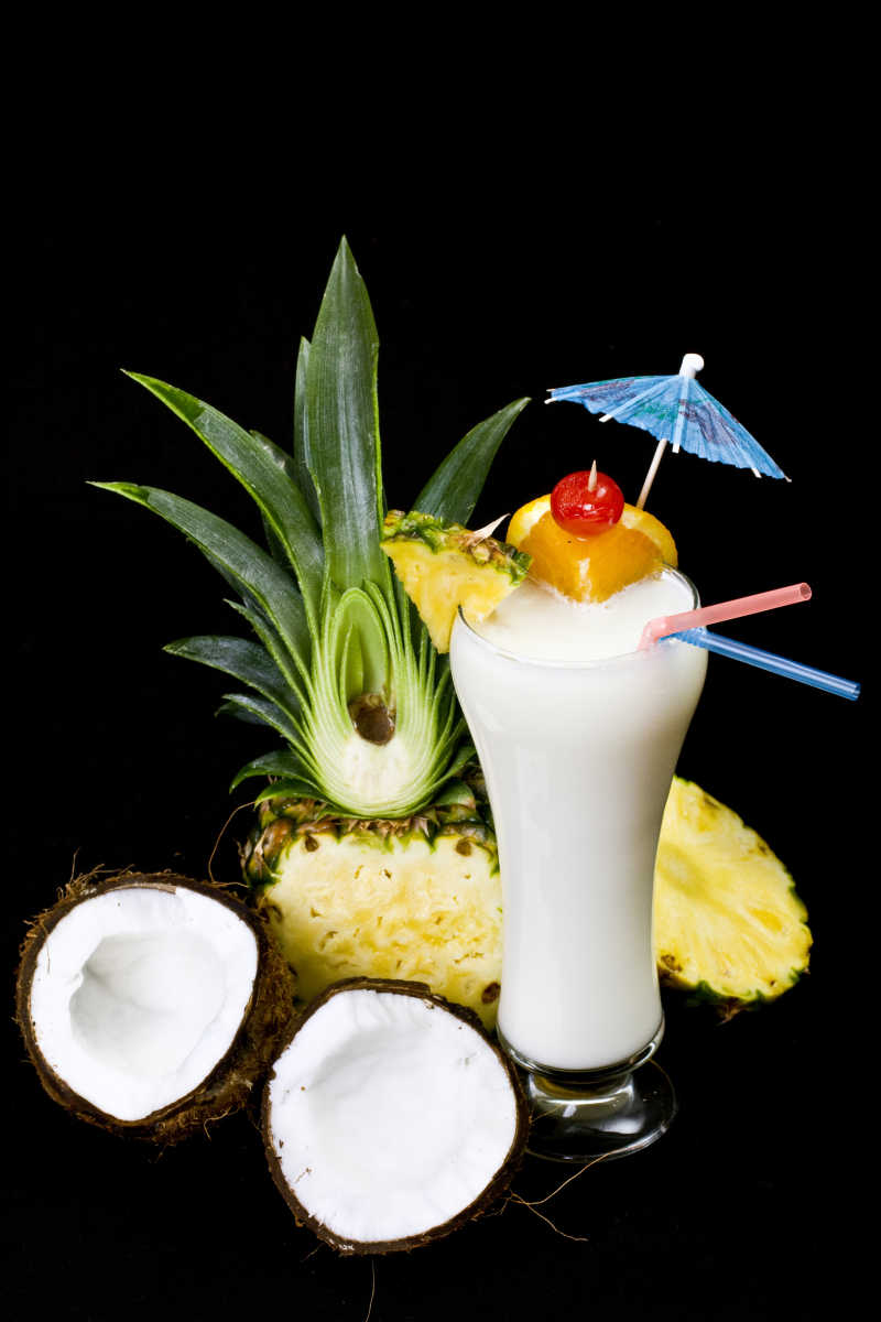 黑色背景下有菠萝和椰子的桌上的白色鸡尾酒