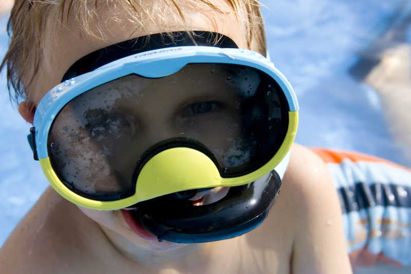 带着潜水镜浮出泳池的小男孩