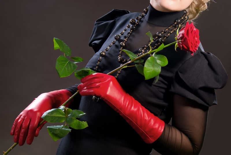 正带着红色皮手套拿着玫瑰花的美女