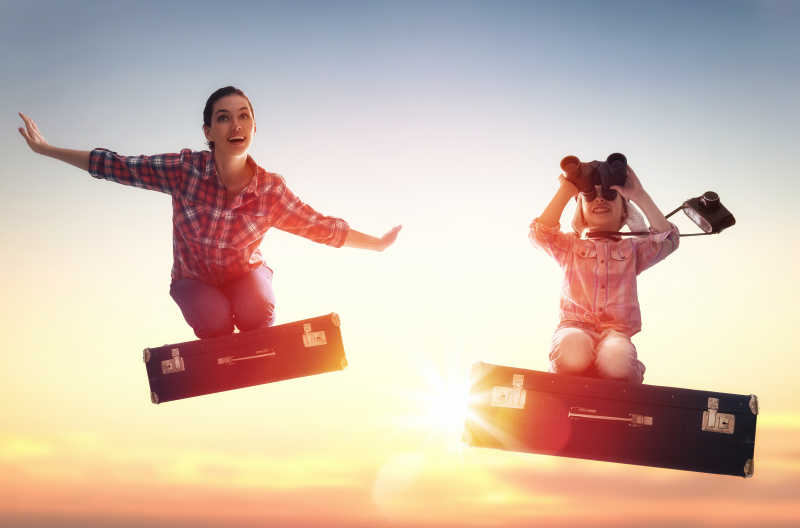 小女孩和她的母亲乘着一个手提箱在日落的背景下飞行