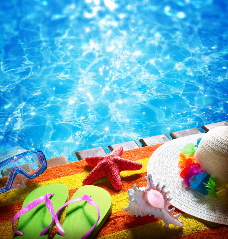 蓝色游泳池边太阳帽拖鞋游泳镜等游泳物品