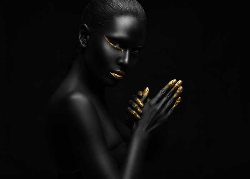 全身漆黑的女人指尖和嘴唇涂着金粉在黑色背景上