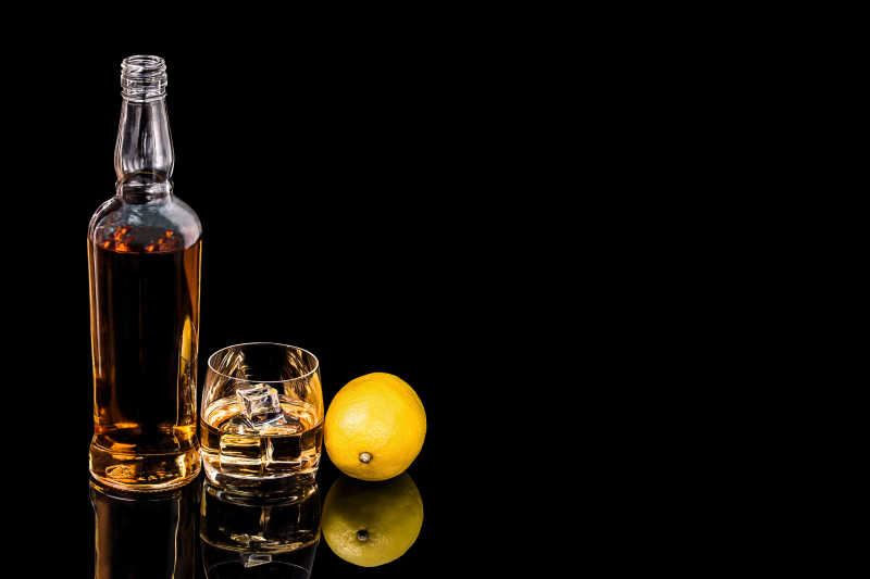 黑色背景下的瓶子和玻璃威士忌和柠檬