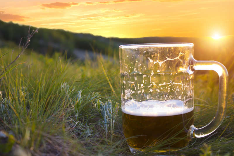 日落的黄色天空下草坪上的一杯冷啤酒