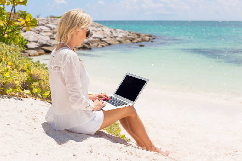 在沙滩上坐在的计算机工作的美女