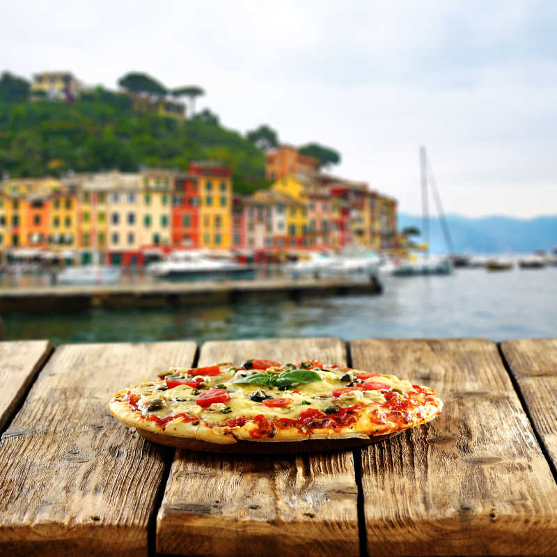 远处的海边城市和近处的木桌上的披萨