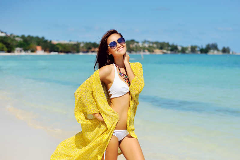  蓝色海边沙滩上穿着白色比基尼披着黄色披肩的美女