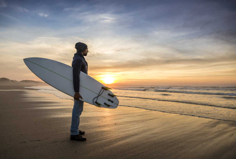 一个冲浪者在日落时用冲浪板看着浪涛