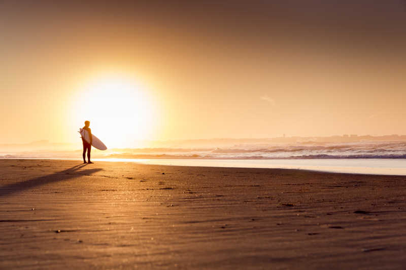 日落时分海滩上的站立的 冲浪者
