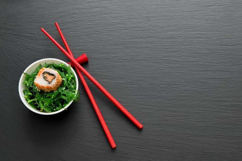 红色筷子旁碗里的寿司和海草卷