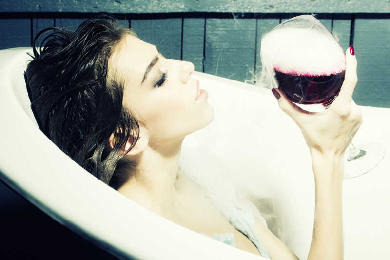 在白色浴缸里享受红酒的美女