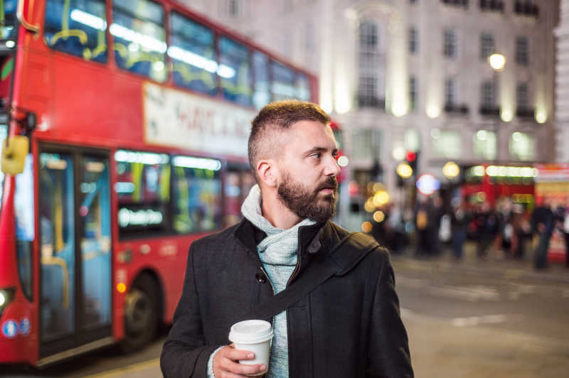 伦敦街头红色巴士背景前带咖啡杯的人