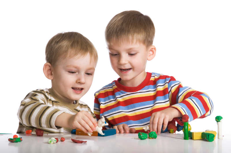 白色背景上在桌上玩橡皮泥的两个金发男孩
