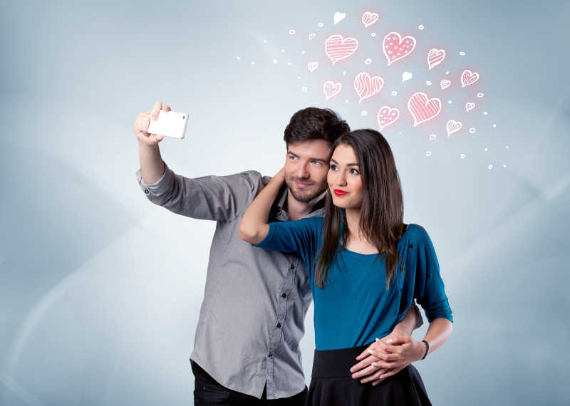 在一个空的清灰墙背景概念前恋爱中的年轻夫妇和绘制红心采取selfie自拍