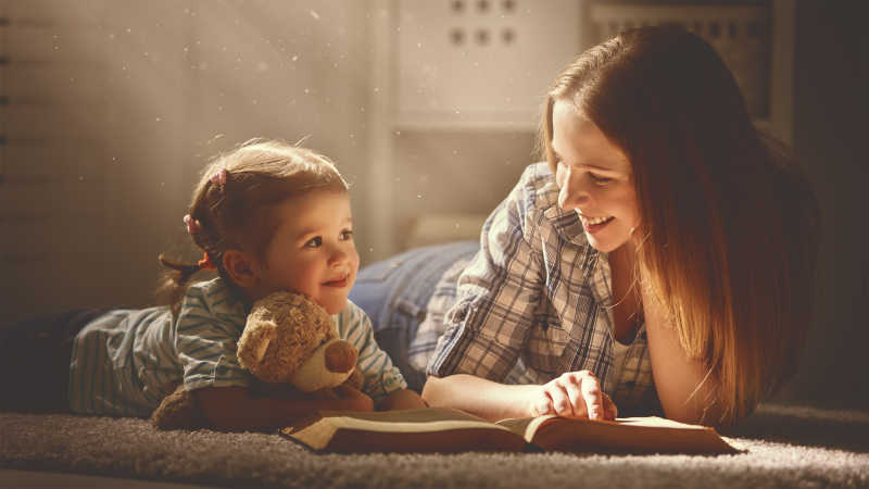 快乐的家庭母亲和女儿晚上在家看书