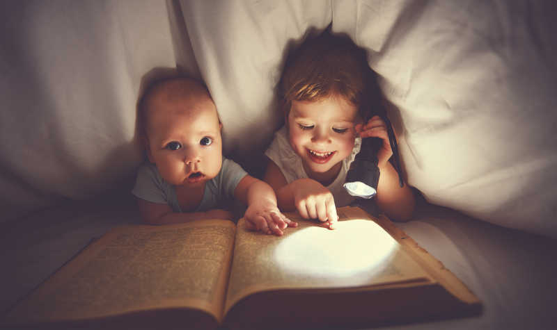 孩子兄弟姐妹在床下用一盏灯看书