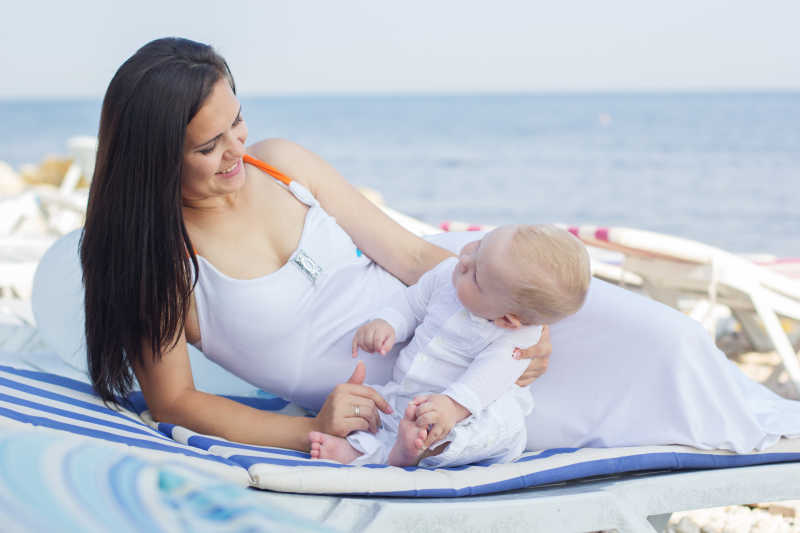 年轻妈妈陪刚出生不久的小婴儿在海滩玩耍