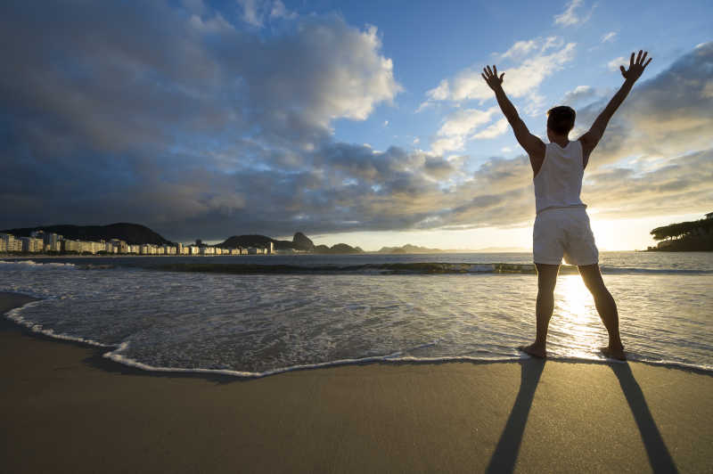 日落沙滩上举着手臂的运动员