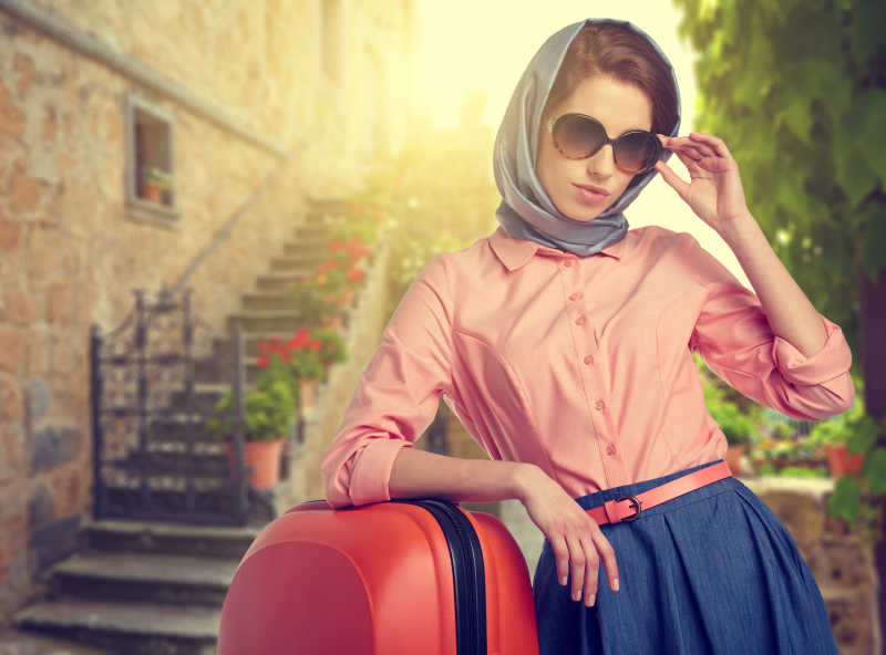 优雅的女人带着一个行李箱走在意大利城市的街道上