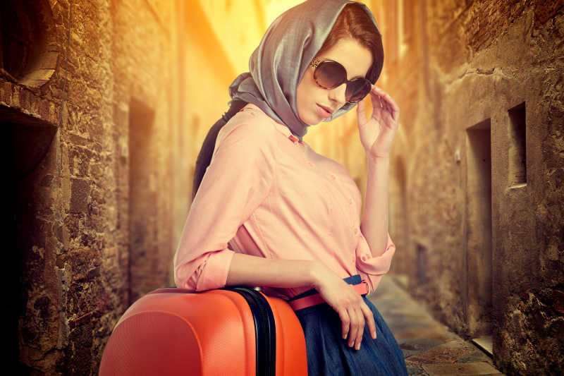 意大利城市街道上有一个橙色行李箱的优雅女人