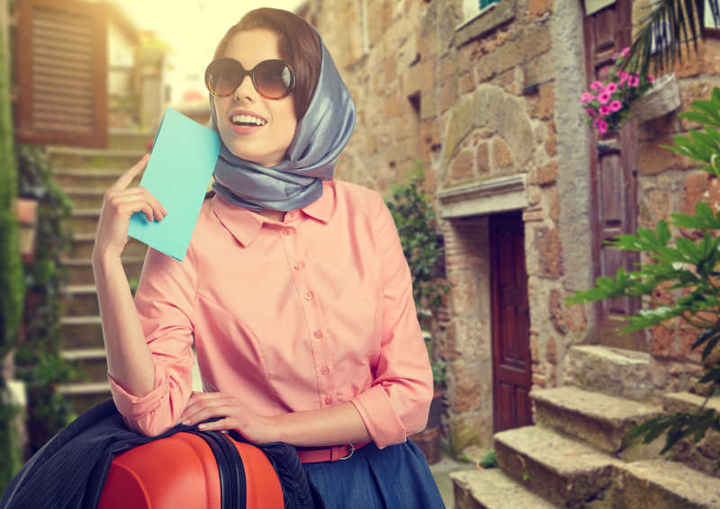 优雅的女人带着行李箱旅行和机票在意大利城市街头