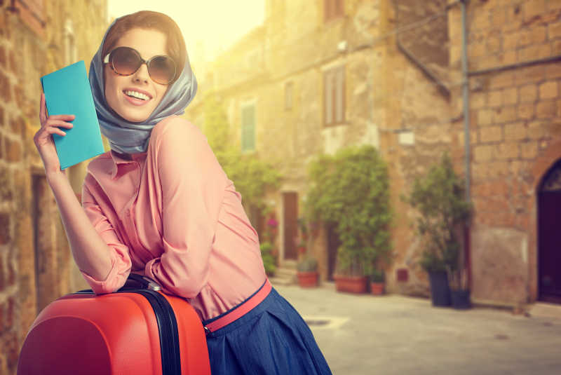 优雅的女人带着一个行李箱和机票在意大利城市街头